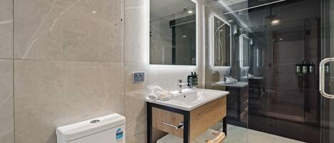 Un baño moderno con ducha de vidrio, lavamanos blanco y tocador de madera.