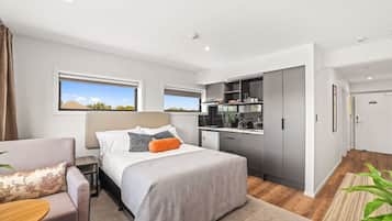 Quarto de hotel moderno com cama, escrivaninha pequena, cozinha compacta e vista para o exterior.