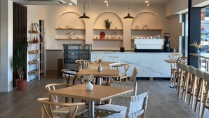 A modern cafe interior with wooden tables and chairs, a coffee bar, and shelves with decorative items. - Golden Hotel (Christchurch)