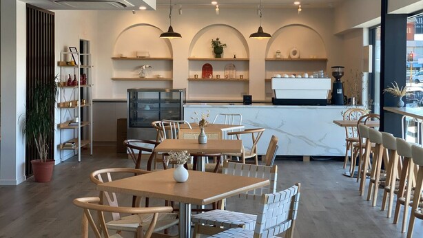 A modern cafe interior with wooden tables and chairs, a coffee bar, and shelves with decorative items. - Golden Hotel (Christchurch)