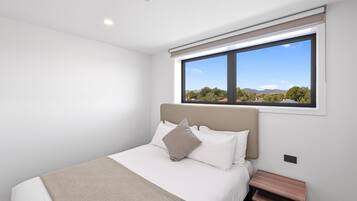 A bedroom with a bed, a nightstand, a window with a view of trees and mountains, and a ceiling light.
