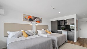 A modern hotel room with two beds, a kitchenette, and a large painting on the wall. - Golden Hotel (Christchurch)