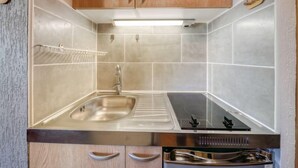 Een kleine keuken met een roestvrijstalen spoelbak, een inbouwfornuis en houten keukenkastjes.