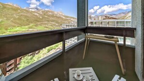 Een balkon met een tafel en stoelen, met uitzicht op een bergachtig landschap en een brug.