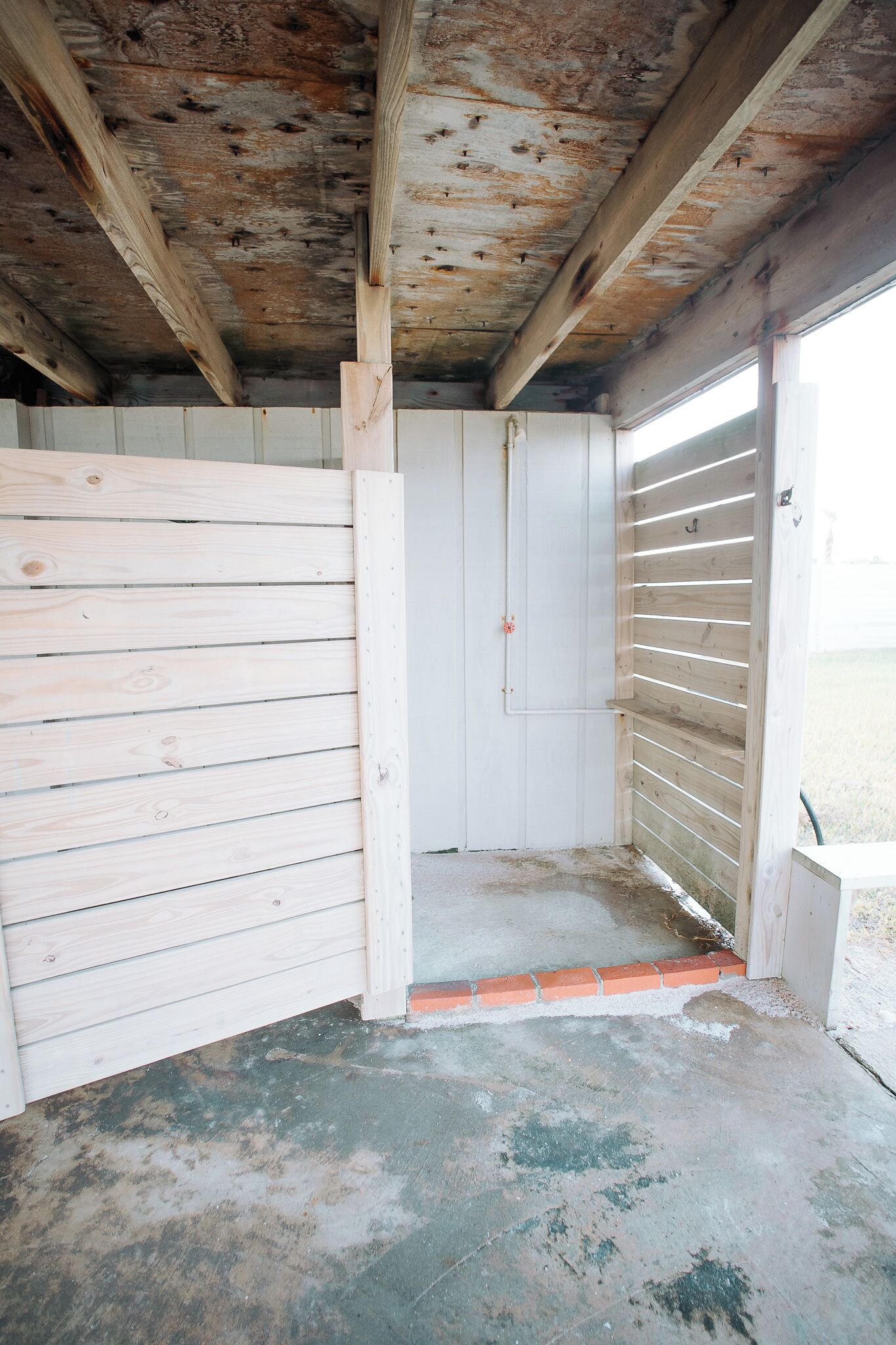 A room with a wooden ceiling, a white door, and a concrete floor.