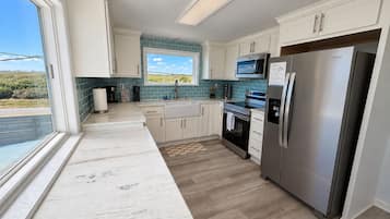 A modern kitchen with white cabinets, a stainless steel refrigerator, a microwave, and a large window offering a view of the outdoors.
