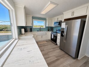 Een moderne keuken met witte kastjes, een roestvrijstalen koelkast, een magnetron en een groot raam met uitzicht op de omgeving.
