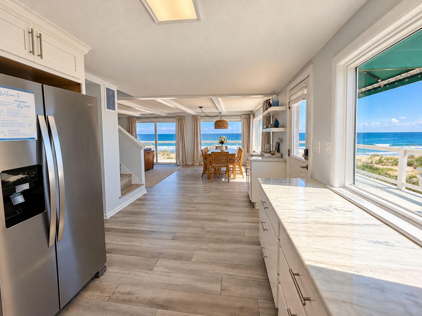 A modern kitchen with a view of the ocean, wooden flooring, and a dining area with a table and chairs.
