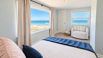 A bedroom with a bed, a chair, a view of the beach, and a door.