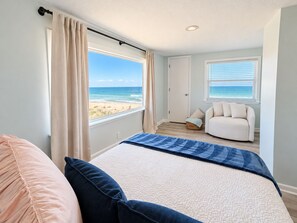 Een slaapkamer met een bed, een stoel, uitzicht op het strand en een deur.