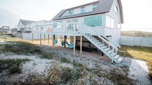 A beachfront house with a wooden deck, a staircase leading to a second floor, and a hammock. - Oceanfront Escape, Grill, Hammocks, Fire Pit, & Stunning Views (Ponte Vedra Beach)
