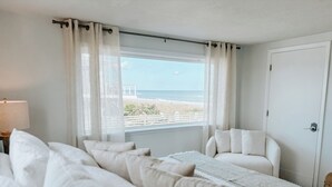 A bedroom with a large bed, a view of the beach, and a white door. - Oceanfront Escape, Grill, Hammocks, Fire Pit, & Stunning Views (Ponte Vedra Beach)
