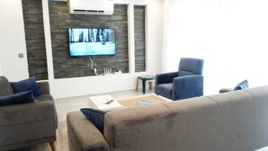 A modern living room with a flat-screen TV mounted on a textured wall, two armchairs, a sofa, and a coffee table.