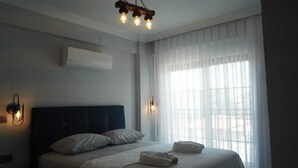 A bedroom with a bed, two wall-mounted light fixtures, a ceiling light, and a window with sheer curtains.