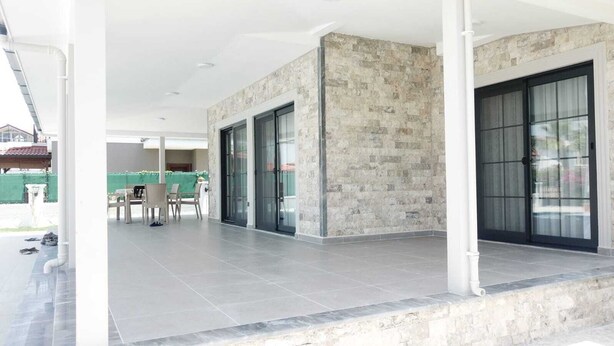 A covered outdoor area with a stone wall, a table with chairs, and a glass door entrance.