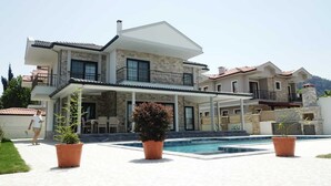 A two-story house with a swimming pool, outdoor seating, and potted plants.