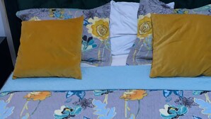 Una cama con colcha de estampado floral, cabecera tapizada en color verde oscuro y dos almohadas amarillentas.