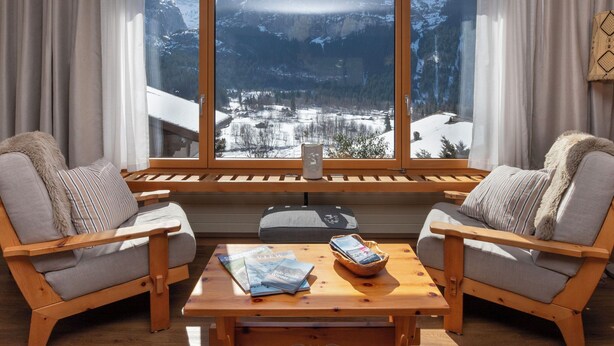 A room with two wooden chairs, a wooden table, and a large window with a view of snow-covered mountains. - SnowKaya Grindelwald by Interhome (Grindelwald)