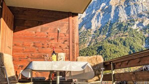 A wooden cabin with a table and chairs, a bottle, and a mug, overlooking a mountainous landscape. - SnowKaya Grindelwald by Interhome (Grindelwald)