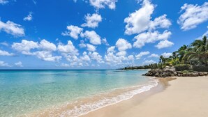 Ein Strand mit klarem türkisblauem Wasser, einem sandigen Ufer und einer Reihe von Palmen.