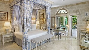 Ein Schlafzimmer mit Himmelbett, Schreibtisch und Stuhl, mit Steinwänden und Blick auf Grünfläche.