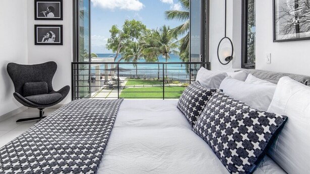 A bedroom with a large bed, a view of the ocean, a balcony, and a chair. - Onyx by Blue Sky Luxury (Weston)