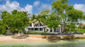 A beachfront property with a large house, palm trees, and a clear view of the ocean. - Onyx by Blue Sky Luxury (Weston)