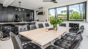 A modern kitchen with a large island, black bar stools, and a dining area with a wooden table and black chairs. - Onyx by Blue Sky Luxury (Weston)