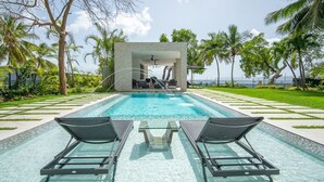 A pool area with two lounge chairs, a covered seating area, and a view of the ocean. - Onyx by Blue Sky Luxury (Weston)