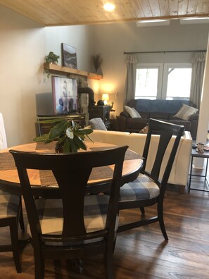 Een gezellige woonkamer met houten plafond, een open haard, een bank en een eettafel met stoelen.
