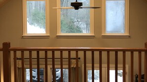 Une pièce avec un plafond en pente, des poutres en bois, un ventilateur de plafond et trois fenêtres.