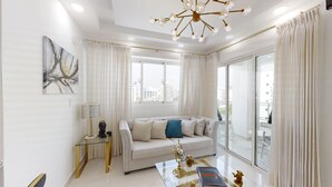 A modern living room with a sofa, a glass coffee table, and a chandelier. - Luxurious 2BR condo with Rooftop, jacuzzi and BBQ (Santo Domingo)
