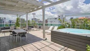 A rooftop terrace with a hot tub, outdoor seating, and a view of the city skyline. - Luxurious 2BR condo with Rooftop, jacuzzi and BBQ (Santo Domingo)