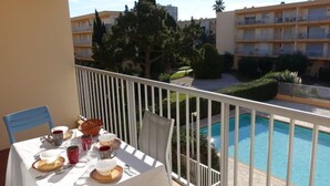 Ein Balkon mit Esstisch, mit Blick auf einen Swimmingpool und einen Gebäudekomplex.