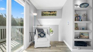 A modern living room with a white armchair, a floor lamp, a bookshelf, and a large window with a view of trees. - Casa Azul Steps from Rio del Mar Beach (Aptos)