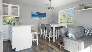 A modern kitchen with white cabinets, a dining area with a white table and chairs, and a gray sofa. - Casa Azul Steps from Rio del Mar Beach (Aptos)
