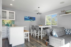 A modern kitchen with white cabinets, a dining area with a white table and chairs, and a gray sofa.