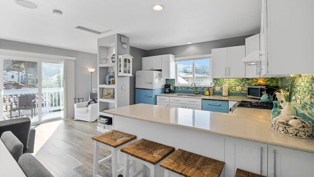 A modern kitchen with a large island, white cabinetry, and a view to the outside. - Casa Azul Steps from Rio del Mar Beach (Aptos)