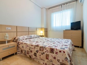 A bedroom with a bed, a nightstand, a dresser, a television, and a window with curtains.