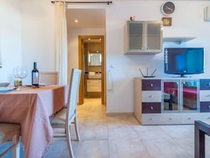 A room with a dining table set for two, a television on a cabinet, and a bathroom visible through an open door.