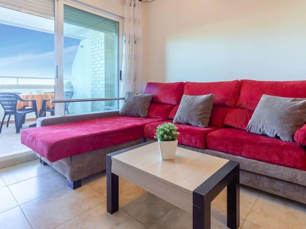 A modern living room with a red sofa, a small table, and a balcony with a view of a building.