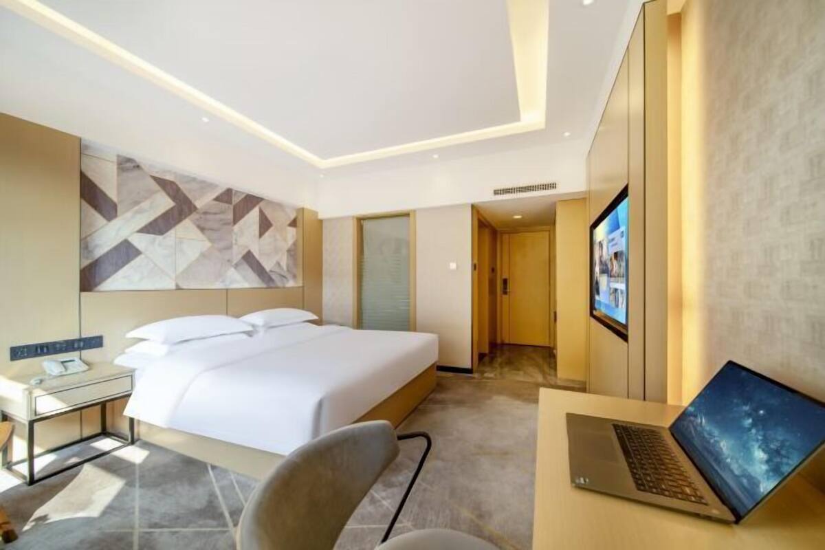Une chambre d’hôtel moderne équipée d’un lit, d’un bureau, d’une chaise et d’un ordinateur portable.