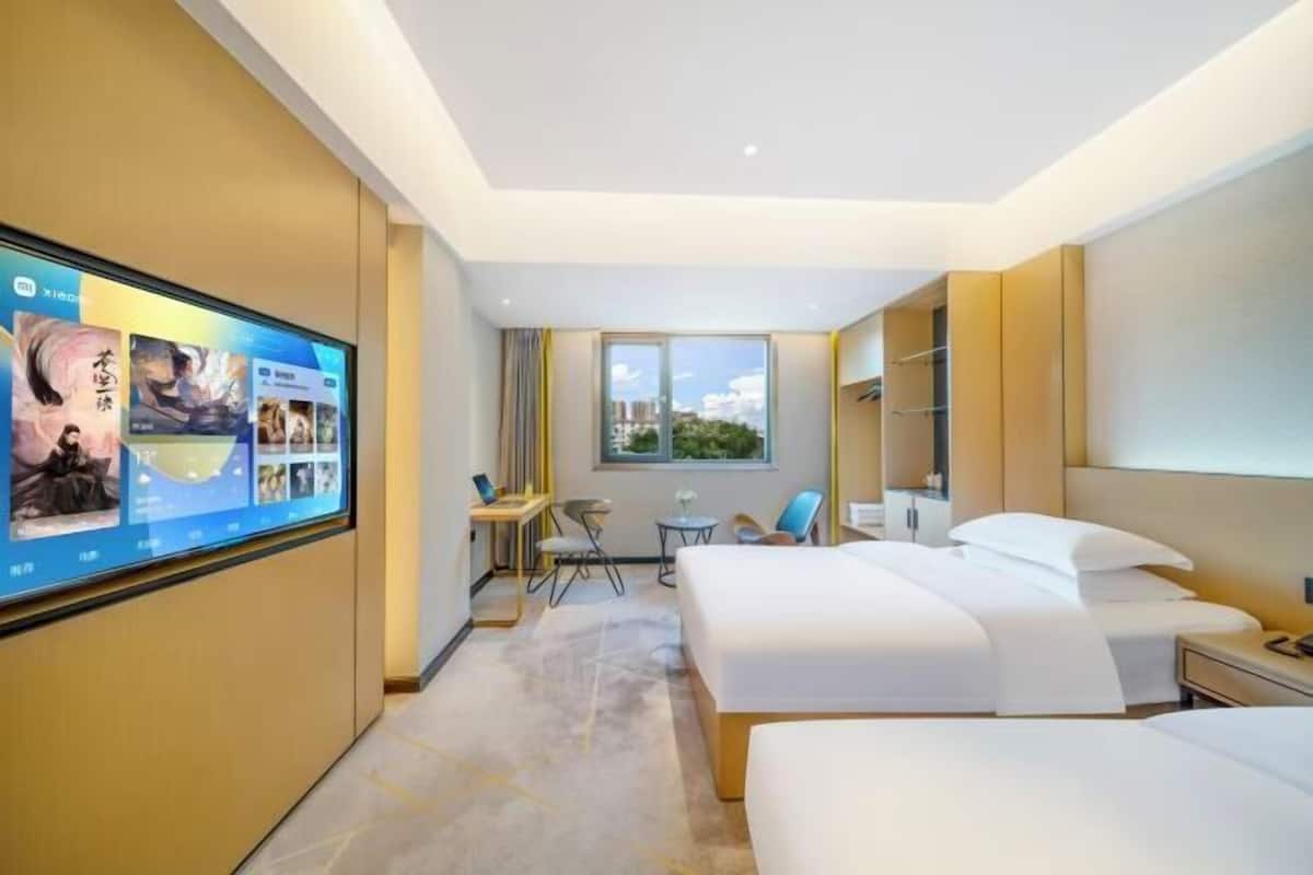 Une chambre d’hôtel dotée d’un grand téléviseur à écran plat fixé au mur, de deux lits, d’un bureau avec une chaise, d’une petite table et d’une fenêtre donnant sur la ville.