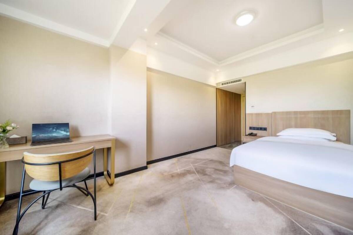 Une chambre d’hôtel comprenant un lit, un bureau avec un ordinateur portable, une chaise et une porte donnant sur une autre pièce.