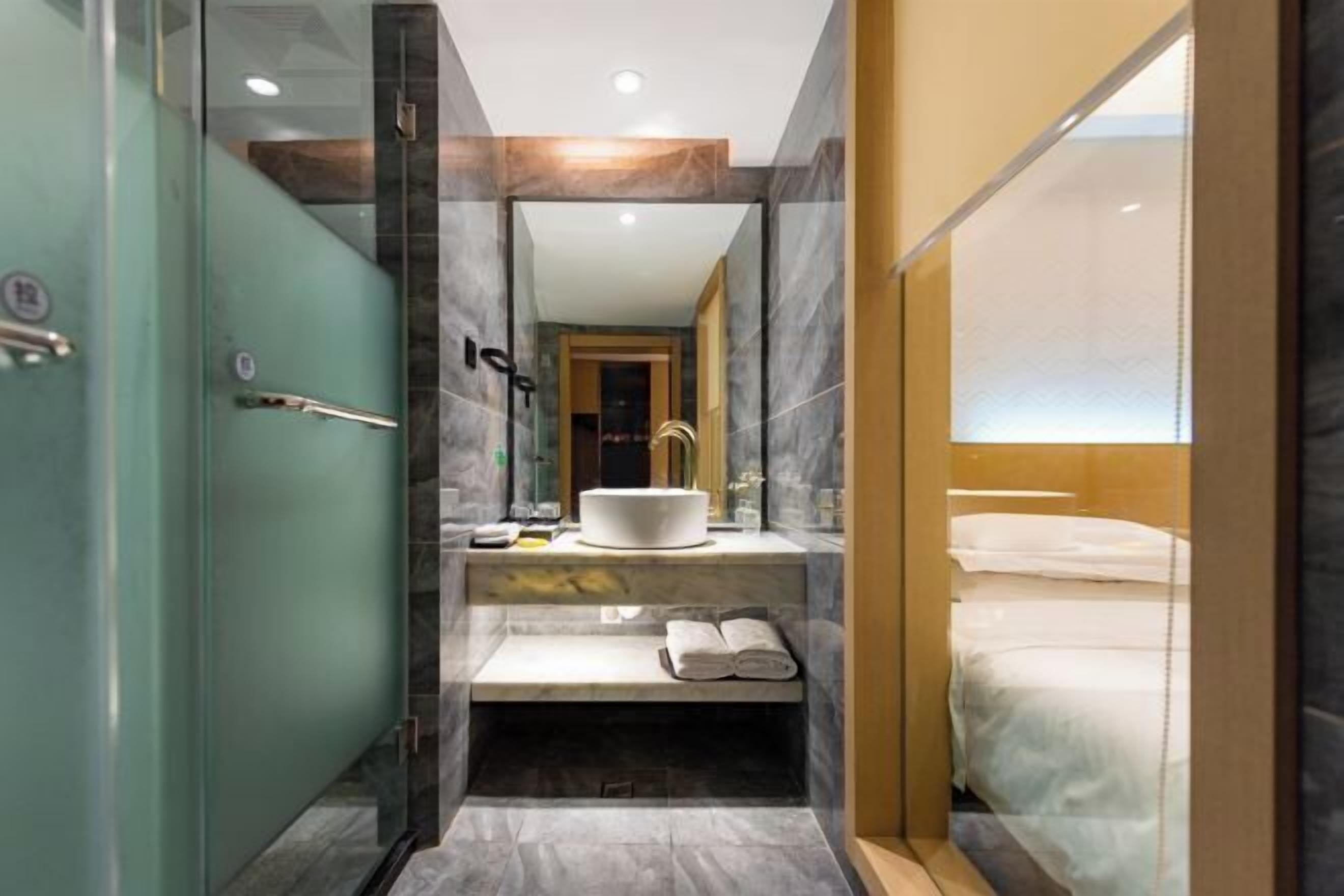 A modern bathroom with a glass-enclosed shower, a sink with a white basin, and a bench with towels.