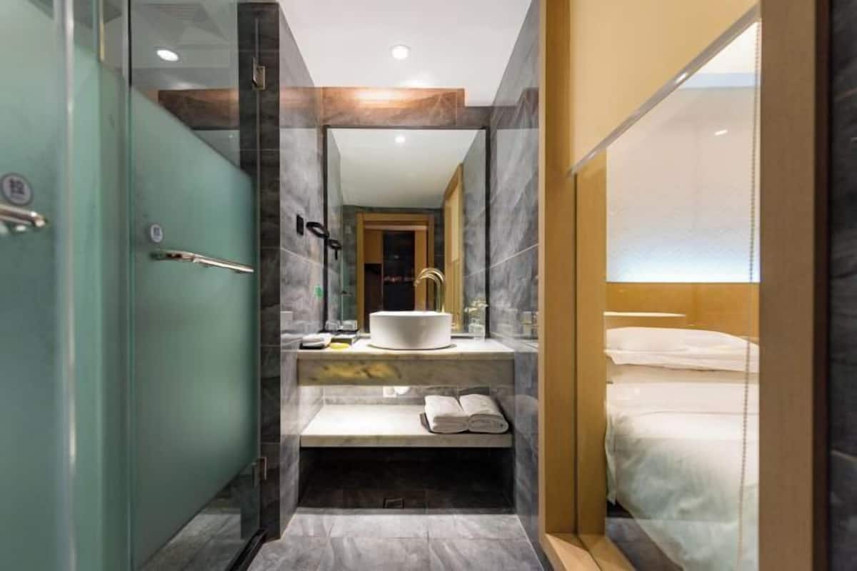 Une salle de bain moderne avec une douche à parois de verre, un lavabo avec un receveur blanc et un banc avec des serviettes.