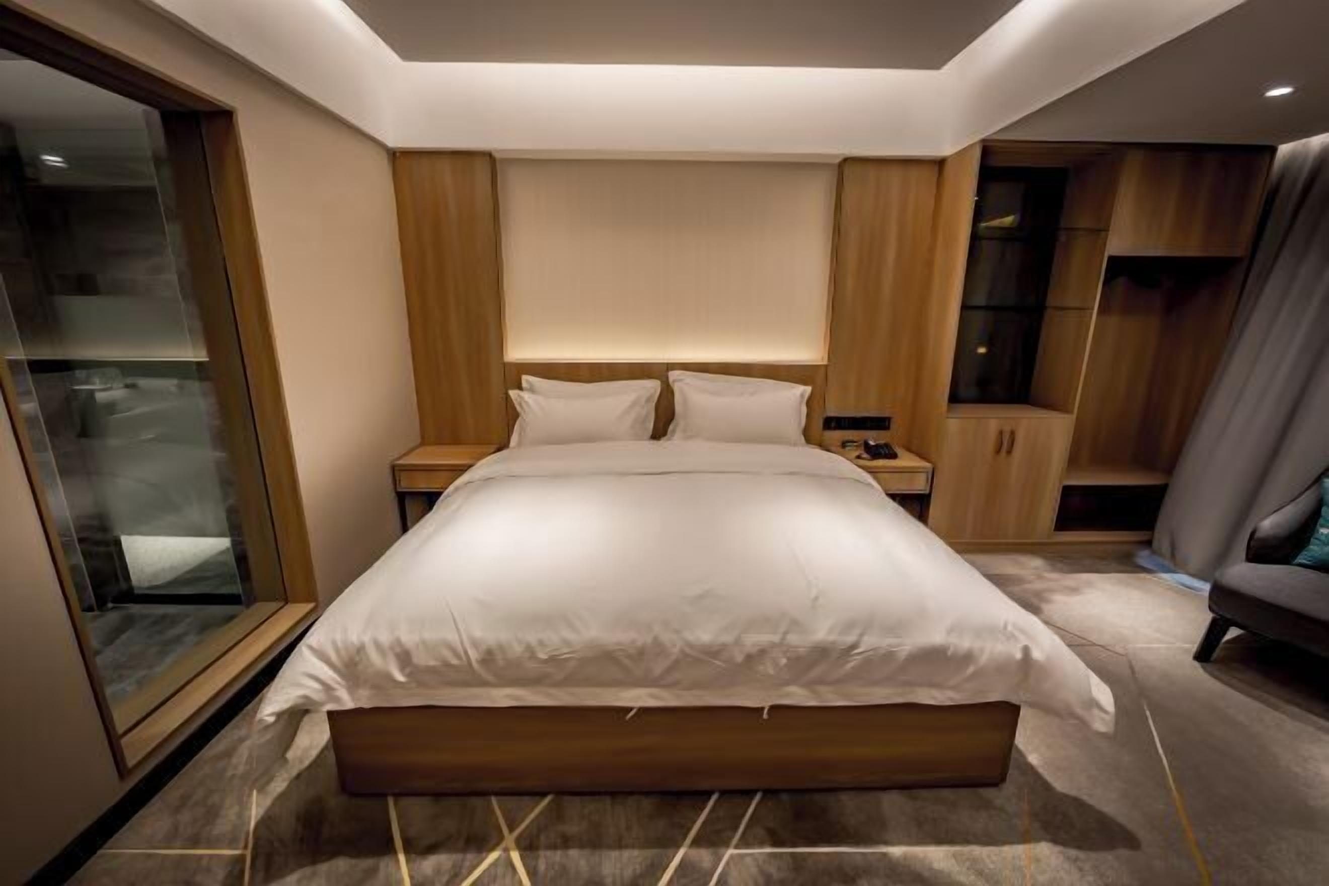 A modern bedroom with a large bed, wooden headboard, bedside tables, and a glass partition.