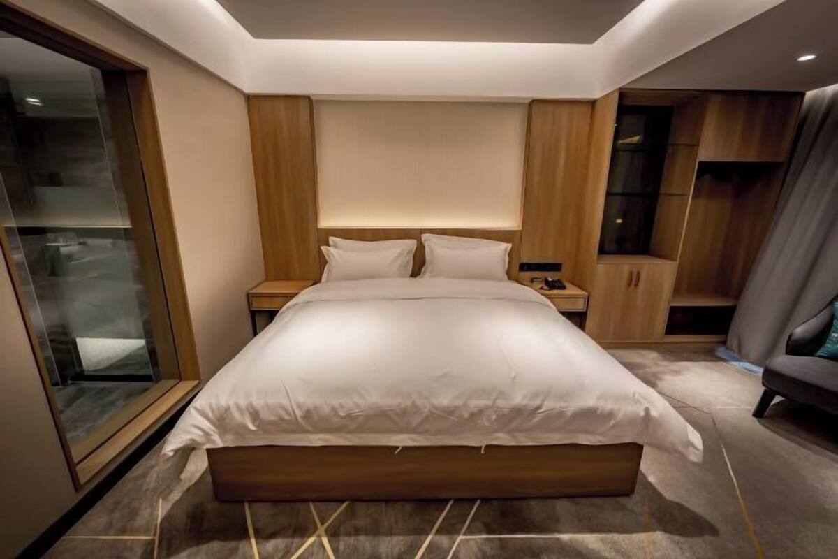 Une chambre moderne avec un grand lit, une tête de lit en bois, des tables de chevet et une cloison en verre.