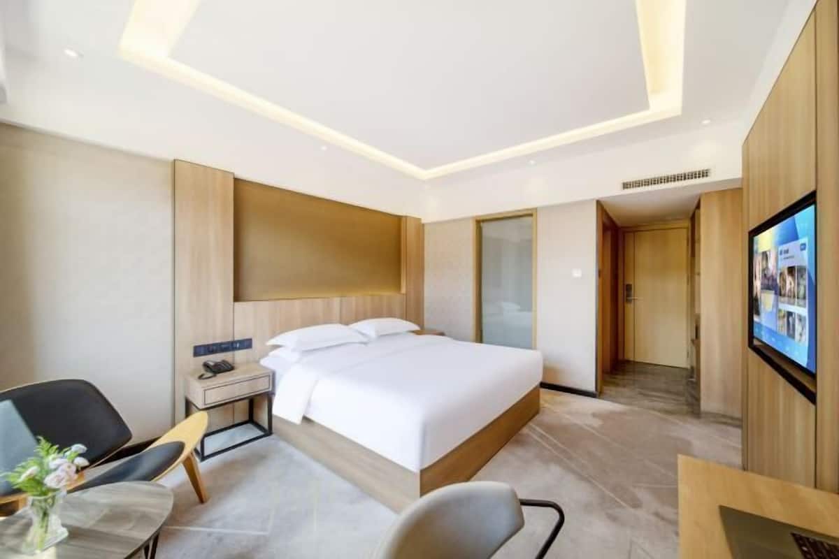 Une chambre d’hôtel moderne, dotée d’un grand lit, d’un bureau, d’une chaise, d’une télévision et d’une petite table sur laquelle est posé un vase.