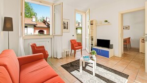 Ein Wohnzimmer mit Sofa, Couchtisch, Fernseher und Blick auf ein Haus durch eine offene Tür.